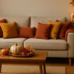Gemütliches Wohnzimmer mit herbstlicher Wohnungsdekoration, warmen Farben, Kissen, Kürbissen und Kerzen.