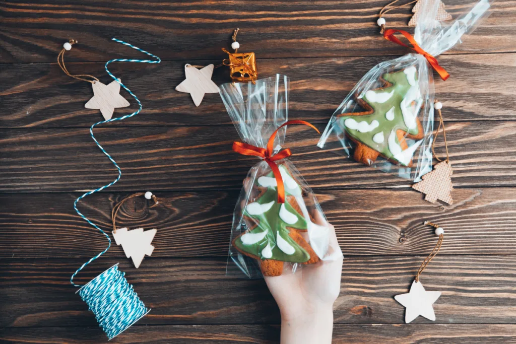 Hand hält weihnachtlich verpackte Plätzchen in Tannenbaumform als Wichtelgeschenk