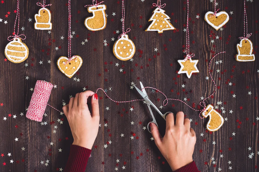 Hände basteln Wichtelgeschenke mit Plätzchenanhängern aus Teig und roter Schnur