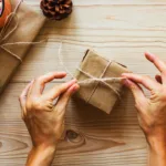 Hände binden Wichtelgeschenk aus braunem Papier mit Juteschnur und Tannenzweig