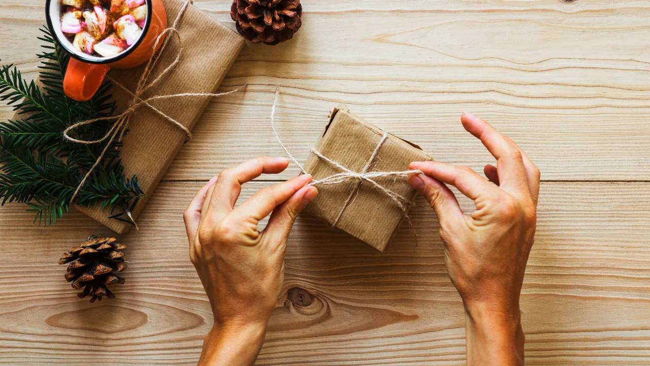 Hände binden Wichtelgeschenk aus braunem Papier mit Juteschnur und Tannenzweig