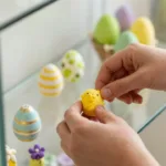 Osterdeko in Glasvitrine mit bunten Eiern, Kükenfigur und gelbem Hasen