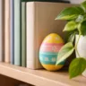 Osterei im Regal versteckt zwischen Büchern und Zimmerpflanze – Ostereierverstecke in der Wohnung entdecken