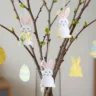 Osterdeko schnell gemacht mit dekorierten Zweigen, Hasenanhängern und bunten Ostereiern in Vase