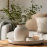 Wohnzimmerdeko aus Keramik mit Vase auf Holztisch im modernen Wohnzimmer mit natürlicher Einrichtung.