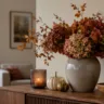 Herbstdeko für das Sideboard mit Vase, Trockenblumen, Kürbissen und Kerzenlicht.