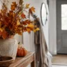 Herbstdeko für den Flur mit Vase, Herbstzweigen, Kürbissen und Laterne auf einer schmalen Konsole.