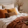 Herbstdeko fürs Schlafzimmer mit Bett, Kissen, Tagesdecke und warmen Naturtönen.