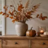 Herbstdeko für die Kommode mit Vase, Kürbissen, Kerze und natürlichen Zweigen im warmen Wohnzimmer.