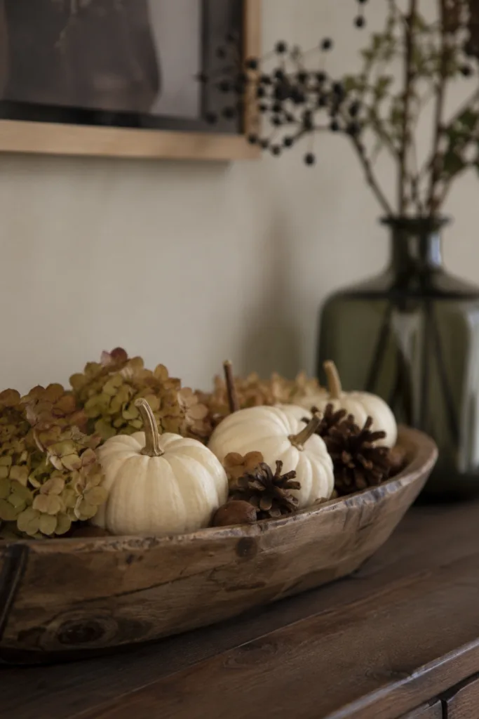 Herbstdeko für das Sideboard mit Kürbissen, Zapfen und Hortensien in einer Holzschale.