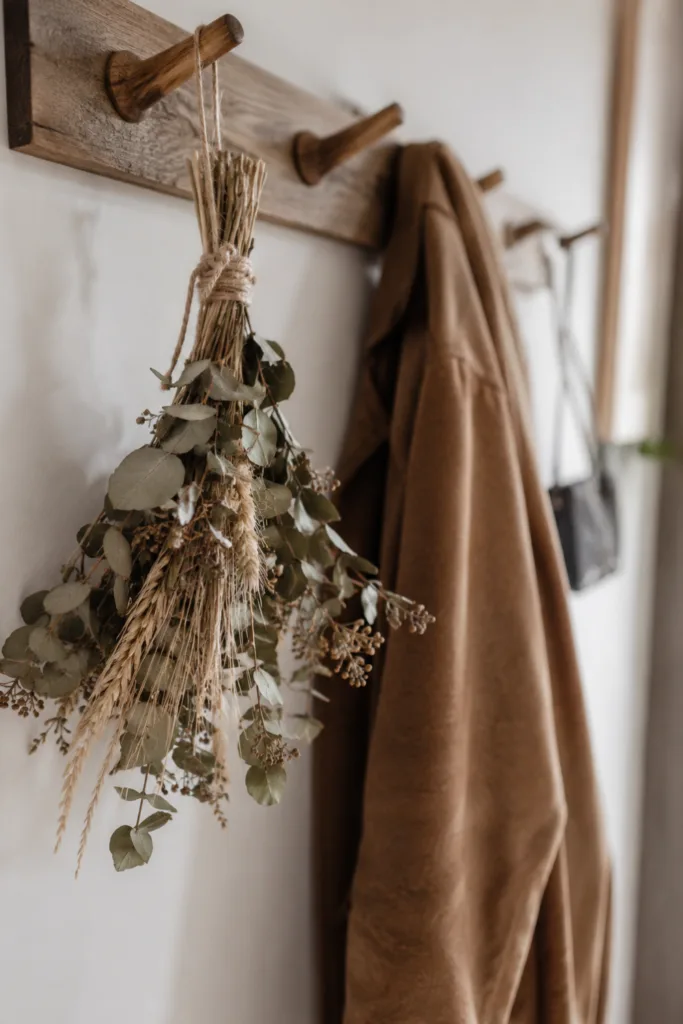 Herbstdeko für die Garderobe mit Trockenblumen, Holzhaken und brauner Jacke im hellen Flur.