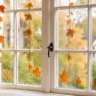 Herbstdeko fürs Fenster mit hängenden Ahornblättern in warmen Herbstfarben vor einem hellen Wohnungsfenster.