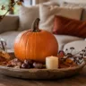 Herbstdeko für den Wohnzimmertisch mit Kürbis, Kerze und Blättern auf einem Holztisch im Wohnzimmer.