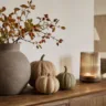 Herbstdeko für die Anrichte mit Vase, Kürbissen und Kerzenglas auf einem Holzsideboard.