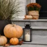 Moderne Herbstdeko auf Treppenstufen mit Kürbissen, Laterne und Pflanzkübel vor einem Hauseingang.