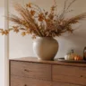 Moderne Herbstdeko für die Kommode mit Keramikvase, Trockenblumen, Kürbissen und Windlicht auf Holzkommode.