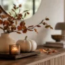 Moderne Herbstdeko fürs Sideboard mit Vase, Kürbis und Kerze auf Holzsideboard im weichen Tageslicht.