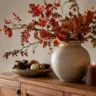 Herbstdeko fürs Sideboard selber machen mit Vase, Zweigen, Kerze und kleinen Kürbissen auf Holzsideboard.