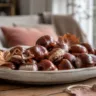 Herbstdeko mit Kastanien basteln: glänzende Kastanien in einer flachen Keramikschale auf rustikalem Holztisch.