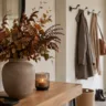 Moderne Herbstdeko für die Garderobe mit Vase, Herbstzweigen, Kerze und ruhiger, aufgeräumter Flurwirkung.