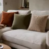 Modern dekoriertes Sofa mit Herbstdeko, Kissen in Rost und Oliv sowie kuscheliger Decke im Wohnzimmer.