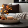 Moderne Herbstdeko für den Wohnzimmertisch mit Tablett, Kerze, Vase und Herbstzweigen im hellen Wohnzimmer.