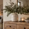 Winterdeko für die Kommode mit Vase, Tannengrün, Kerze und natürlicher Deko im warmen Wohnraum.