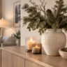 Winterdeko fürs Sideboard mit Vase, Tannenzweigen, Kerzen und Zapfen in warmem Wohnraum.