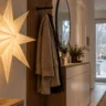 Weihnachtsdeko für die Garderobe mit leuchtendem Papierstern, Holzgarderobe und dezenten Tannenzweigen.