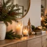 Weihnachtsdeko für das Sideboard mit Tannenzweigen, Kerzen, Holzdeko und warmem Licht.