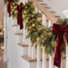 Weihnachtsdeko fürs Treppengeländer mit roten Samtschleifen, grünen Tannenzweigen und warmweißer LED-Lichterkette.
