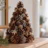Kleiner Weihnachtsbaum aus Tannenzapfen mit weißen Akzenten auf einer Holzkommode neben einer Kerze.