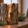 Rustikales Windlicht aus Baumrinde mit warmem Licht, Tannenzweigen und Zapfen auf einer winterlichen Fensterbank.