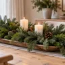 Längliche Holzschale mit frischen Tannenzweigen, weißen Kerzen und Zapfen auf einem weihnachtlich dekorierten Esstisch.