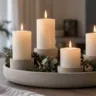 Modernes Adventsgesteck mit vier unterschiedlich hohen weißen Kerzen, Eukalyptus und Tannengrün in einer Keramikschale.