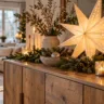 Weihnachtliches Sideboard mit leuchtendem Papierstern, Kerzen, Tannenzweigen und Zapfen im gemütlichen Wohnzimmer.